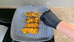 Grilling marinated chicken skewers on a hot pan grill. 2 of 4 skewers show lovely charred marks