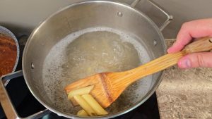 a pot of penne pasta boiling with a few pulled out for "al dente" check