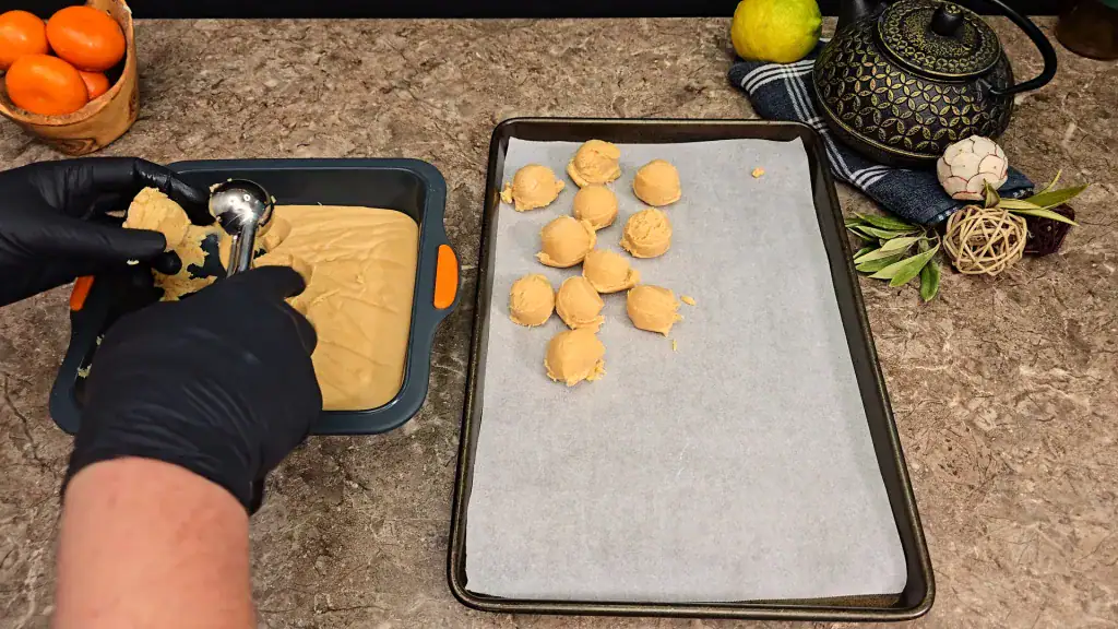 A row of perfectly rolled, chilled peanut butter fudge balls on a baking sheet lined with paper.