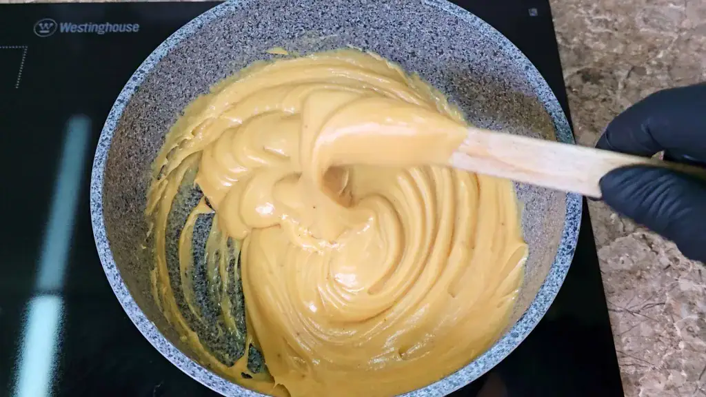 The peanut butter fudge mixture thickening in the pot, with a spatula pulling it away from the side.
