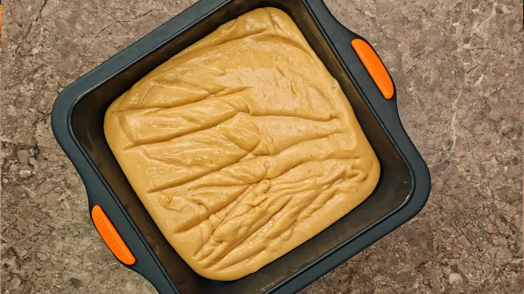 The thick, cooked fudge in a silicone tray, ready for a piece of plastic wrap pressed onto the surface.