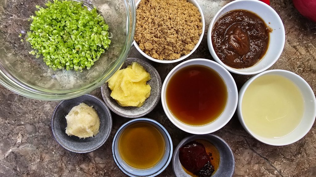 Top-down view of mis en place ingredients for Nam Jim Jaew including tamarind paste, brown sugar, fish sauce, rice vinegar, and finely chopped coriander roots.