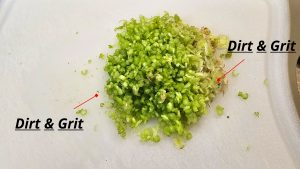 Finely chopped green coriander roots and stems on a white cutting board, prepared as the aromatic base for a Thai dressing.