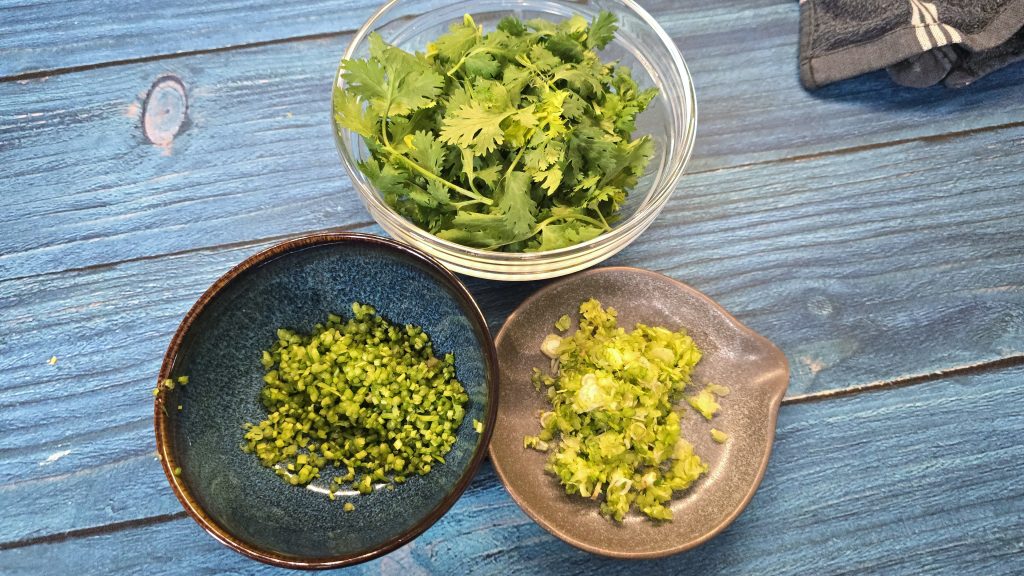 Three ceramic bowls showcasing the separated coriander leaves, chopped stems, and cleaned root base.