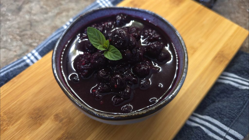 The finished Toffee and Spiced Mixed Berry Compote garnished with a fresh mint sprig in a ceramic bowl.